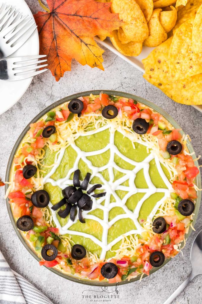 Spider Web 7 Layer Dip is just what your Halloween needs! A spooky little olive spider sits atop a sour cream spider web on layers of meat, beans, cheese, guacamole, and more!