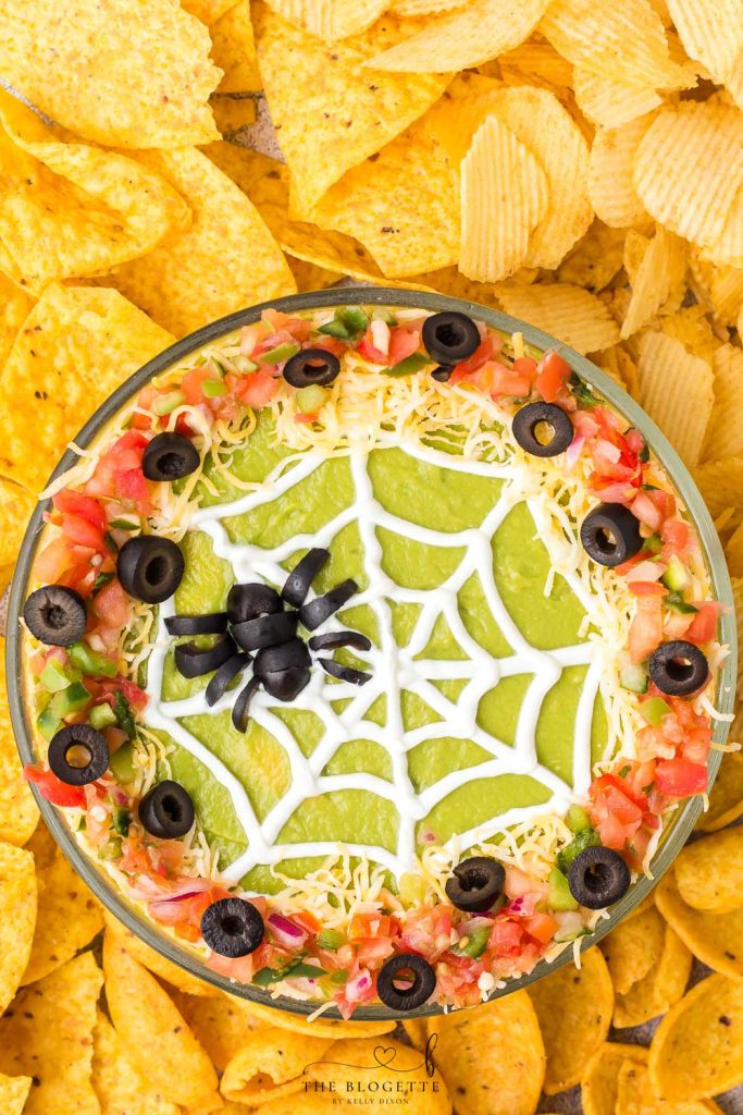 Spider Web 7 Layer Dip is just what your Halloween needs! A spooky little olive spider sits atop a sour cream spider web on layers of meat, beans, cheese, guacamole, and more!